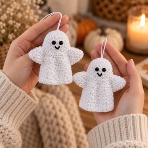 May include: Two white crocheted ghost ornaments featuring black bead eyes and a stitched black mouth. Each ghost has a small white string loop at the top for hanging. The figures are crafted with a textured yarn finish and have a rounded head.