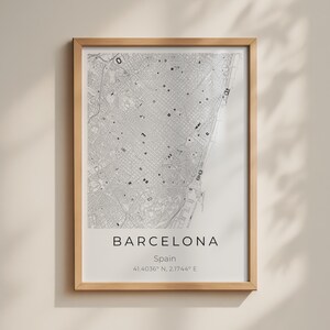 May include: A framed wall art print featuring a detailed black and white street map of Barcelona, Spain. The print includes the text BARCELONA, Spain, and the coordinates 41.4036° N, 2.1744° E centered below the map in a clean font.
