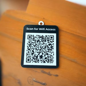 May include: A rectangular black and white sign featuring a QR code and the text Scan for Wifi Access printed in white. The sign has a small circular hole at the top center for hanging, providing a clear visual indicator for wireless network access.
