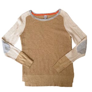 Könnte beinhalten: Beigefarbener Pullover mit Rundhalsausschnitt und langen Ärmeln. Die Ärmel sind hellbeige mit grauen Ellbogenpatches. Der Halsausschnitt hat eine graue Einfassung mit orangefarbenem Akzent. Der Pullover hat einen gerippten Saum und Bündchen.