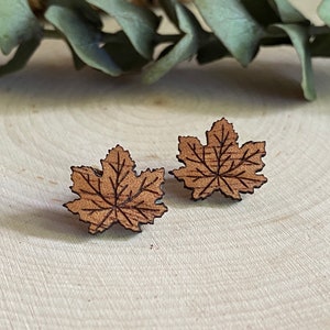 May include: A pair of wooden earrings shaped like maple leaves. The leaves are a light brown color and have a detailed design.