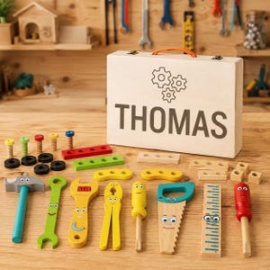 May include: A wooden toy tool set featuring a light-colored wooden carrying case with an orange handle, the name THOMAS, and a gear icon. The set includes various wooden tools with painted faces, including a hammer, wrench, pliers, screwdriver, saw, and ruler, along with assorted wooden bolts, nuts, and connector pieces.