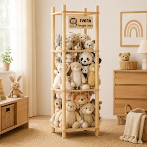 Könnte beinhalten: Ein hohes Spielzeugregal aus hellem Holz mit vertikalen Spanndrähten, die eine Sammlung verschiedener Plüschtiere halten. Ein rechteckiges Holzschild oben zeigt eine Löwenillustration und den Text EVARA Snuggle Safari.