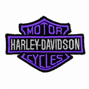 May include: A shield-shaped embroidered patch featuring the Harley-Davidson Motor Cycles logo. The design includes purple stitching on a black background with the text MOTOR, HARLEY-DAVIDSON, and CYCLES in a bold, stylized font with silver-grey lettering.