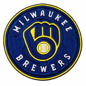 May include: A circular embroidered patch featuring the Milwaukee Brewers logo in blue, yellow, and white. The design displays a baseball glove forming the letter M with a baseball in the center, surrounded by the text MILWAUKEE BREWERS.