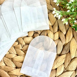 May include: A collection of small, translucent white glassine envelopes with rounded top flaps. These rectangular paper pouches feature a semi-transparent finish and a simple fold-over design, presented as a group of individual units for storage.