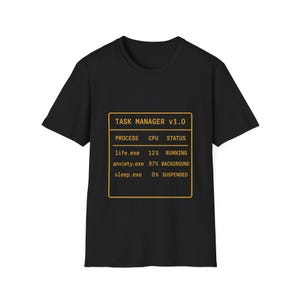 May include: A black short-sleeved t-shirt featuring a yellow graphic of a computer task manager window. The text reads: TASK MANAGER v1.0, PROCESS, CPU, STATUS, life.exe 12% RUNNING, anxiety.exe 97% BACKGROUND, and sleep.exe 0% SUSPENDED.