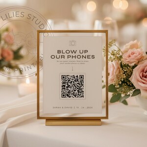 May include: A vertical rectangular gold metal frame holding a white sign with black text that reads BLOW UP OUR PHONES, followed by instructions, a QR code, and the names SARAH & DAVID with the date 10.24.2026 printed at the bottom of the card.