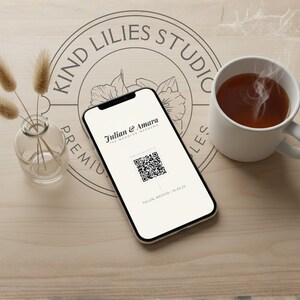 Puede incluir: Un teléfono inteligente que muestra una invitación de boda con el texto Julian & Amara, The Wedding Weekend y un código QR, junto a un pequeño jarrón de cristal con tallos de hierba seca y una taza de cerámica blanca con una bebida humeante.