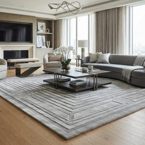 May include: A living room featuring a large gray area rug with a geometric pattern, a curved gray sofa, two beige armchairs, a dark wood coffee table, a fireplace with a television above it, and light wood flooring throughout the space.