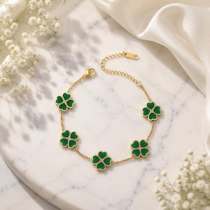Pode incluir: Uma pulseira de corrente em tom dourado com cinco berloques de trevo de quatro folhas espaçados uniformemente. Cada berloque de trevo é preenchido com um esmalte verde vibrante e contornado em ouro. A pulseira inclui uma corrente fina e fecho lagosta.
