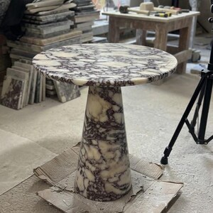 May include: A round side table crafted from white and dark purple veined marble. The table features a circular top supported by a single, wide, conical pedestal base that tapers toward the top, showcasing a consistent natural stone pattern throughout.