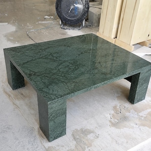 May include: A square coffee table crafted from dark green marble with prominent black veining. The table features a polished, reflective surface and four thick, block-style legs that provide a sturdy base for the flat, smooth tabletop.