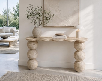 Può includere: Una consolle in travertino beige con un lungo piano dai bordi smerlati, sostenuta da due colonne verticali composte ciascuna da tre sfere sovrapposte. La superficie in pietra naturale presenta una finitura porosa e testurizzata in toni neutri.