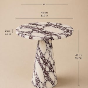 May include: A Calacatta Viola marble side table with a circular top and a conical base. The table features white stone with deep purple veining. Dimensions are 17.7 inches in diameter, 15.7 inches in height, 0.8 inches thick, and a 7.9 inch base.