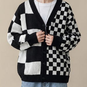 May include: A long-sleeve V-neck cardigan featuring a split design with large black and white checkerboard patterns on one side and smaller black and white checkerboard patterns on the other, finished with a black button-down front closure.