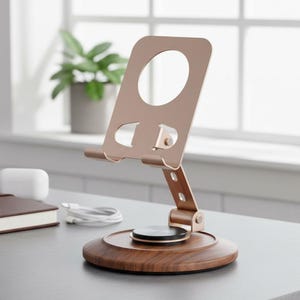 May include: A rose gold metal phone stand with an adjustable arm and a circular cutout, mounted on a round dark wood grain base. The stand features a rotating hinge mechanism and a flat support ledge for a mobile device, providing a stable platform.