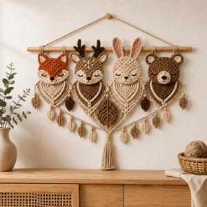 May include: A macrame wall hanging featuring four crocheted animal heads: a fox, a deer, a rabbit, and a bear. Each animal is attached to a wooden dowel and sits above a macrame leaf-shaped design with small wooden beads and a central tassel.
