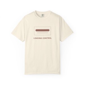 Può includere: Una t-shirt a maniche corte color crema con una grafica rettangolare sul petto. All'interno del rettangolo c'è una barra di caricamento orizzontale con segmenti rosso scuro e il testo LOADING CONTROL in lettere maiuscole rosso scuro.