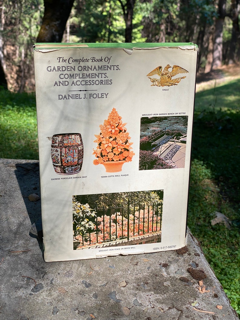 Puede incluir: La contraportada de un libro titulado "The Complete Book of Garden Ornaments, Complements, and Accessories" de Daniel J. Foley. La portada presenta im&aacute;genes de varios ornamentos de jard&iacute;n, incluyendo un asiento de jard&iacute;n de porcelana china, una placa de pared de terracota, un banco de jard&iacute;n de hierro forjado o un conjunto de asientos, y una valla de hierro forjado en una pared de ladrillo.