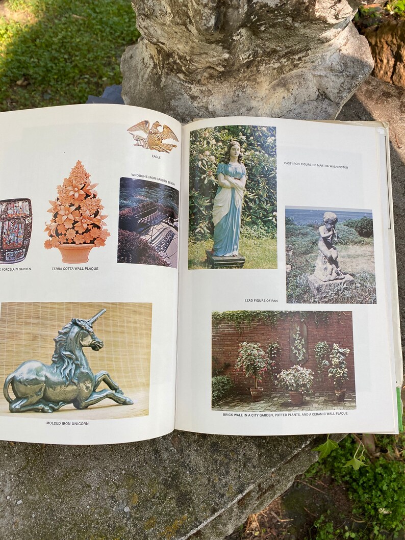 Puede incluir: Un libro abierto en una p&aacute;gina que muestra varios elementos de decoraci&oacute;n de jard&iacute;n, incluyendo una placa de pared de terracota, un banco de jard&iacute;n de hierro forjado, una figura de Martha Washington de hierro fundido, una figura de Pan de plomo, un unicornio de hierro moldeado y una pared de ladrillo con plantas en macetas y una placa de pared de cer&aacute;mica.