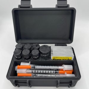 May include: A black rectangular hard-shell carrying case containing medical supplies. Inside are several small glass vials with black caps, a stack of Alcohol & Chlorhexidine Prep pads, and three U-100 insulin syringes with orange caps.