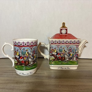 Puede incluir: Una taza de cerámica y una tetera a juego con una colorida ilustración de una carrera de caballos con jinetes y espectadores. Ambas piezas están decoradas con un patrón de techo rojo, un motivo de torre de reloj y el texto A Day at the Races.