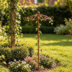 Puede incluir: Un enrejado de jardín de metal color óxido con una varilla vertical central rematada por un marco curvo en forma de paraguas con extremos decorativos en espiral. La estructura está diseñada para plantas trepadoras y tiene hiedra verde.