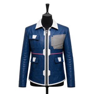 May include: A blue leather jacket featuring a white collar, a central silver zipper, and white trim accents. The jacket includes two chest pockets, two lower pockets, a grey geometric patch on the left chest, and a thin horizontal pink stripe.