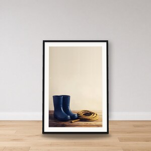 Könnte beinhalten: Ein Paar dunkelblaue Gummistiefel stehen aufrecht auf einer Holzoberfläche neben einem aufgerollten Stück dickem, beigefarbenem Seil. Die Stiefel haben eine glatte Oberfläche und eine abgerundete Spitze, während das Seil eine gedrehte Struktur aufweist.