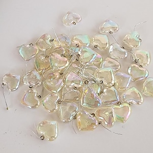 May include: A collection of small, heart-shaped charms with an iridescent, pearlescent finish. Each heart is made of a clear material that reflects light with rainbow hues and includes a thin, silver-colored metal wire loop for attachment.