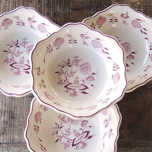 May include: Four white ceramic bowls with scalloped edges and a floral design in shades of purple. The bowls are arranged on a weathered wooden surface, showcasing a vintage aesthetic. Each bowl features a unique floral pattern.