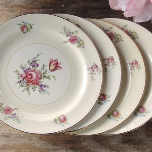 May include: Set of four white ceramic dinner plates with a floral design featuring pink, red, and blue flowers. The plates have a gold rim.