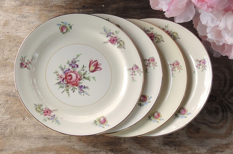 May include: Set of four white ceramic dinner plates with a floral design featuring pink, red, and blue flowers. The plates have a gold rim.