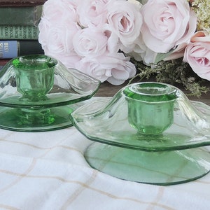 May include: Two green glass candle holders with a fluted design. The candle holders are on a white and brown checkered tablecloth.