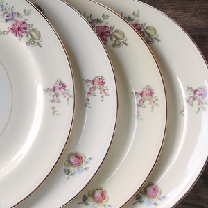 May include: Four white ceramic dinner plates with a gold rim and a floral design in shades of pink, purple, and green.