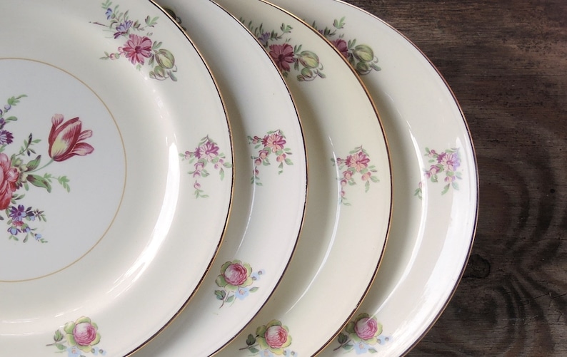 May include: Four white ceramic dinner plates with a gold rim and a floral design in shades of pink, purple, and green.