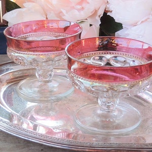 May include: Two clear glass stemmed dessert dishes with a red rim on a silver serving tray. The dishes are empty and the tray is on a wooden surface.