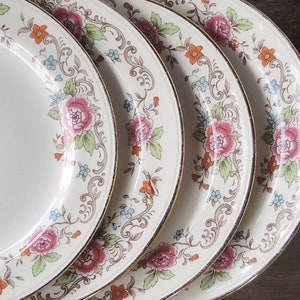 May include: Set of four white ceramic plates with a gold rim and floral pattern in shades of pink, orange, and blue.