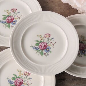May include: Four white ceramic plates with floral designs. Each plate features a different arrangement of pink, red, and yellow flowers with green leaves.