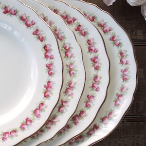 May include: Four white ceramic plates with a gold rim and a pink rose pattern.