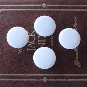 May include: Four white round ceramic knobs on a brown leather-bound book.