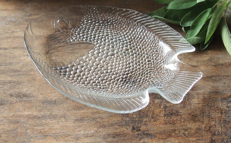 May include: A clear glass fish-shaped serving dish with a textured surface. The dish is designed to resemble a fish with scales and fins.