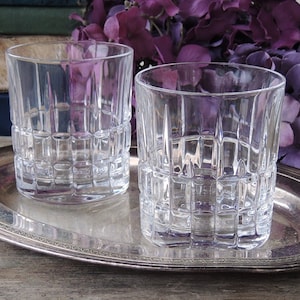 May include: Two clear glass tumblers with a square patterned design sit on a silver tray. The tray is on a wooden surface.