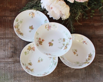 May include: Four white ceramic bowls with a floral pattern of brown and green leaves. The bowls are arranged in a circle on a wooden surface.
