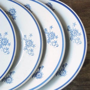 May include: Four white ceramic plates with blue floral designs stacked on top of each other.