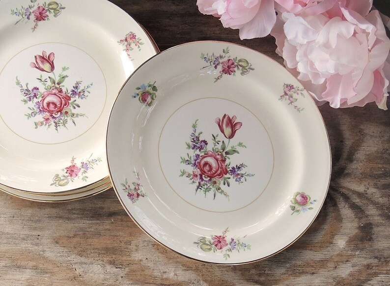 May include: Set of three white ceramic plates with a gold rim and floral design featuring pink and red roses, tulips, and green leaves.