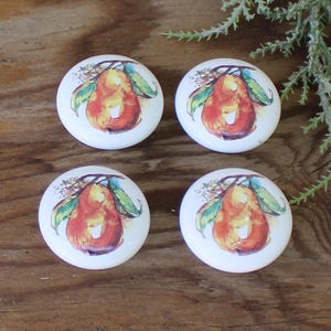 May include: Four white ceramic knobs with a pear design. Each knob features a pear with a red, orange, and yellow color scheme, surrounded by green leaves and white blossoms.
