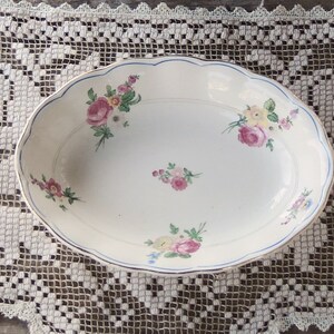 May include: A white oval serving dish with a blue and gold trim. The dish is decorated with a floral pattern in shades of pink, yellow, and green.