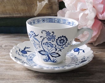 May include: A white teacup and saucer with a blue floral pattern. The cup has a scalloped rim and a handle. The saucer has a scalloped edge.